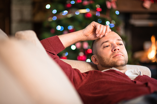 Man looking tired on the couch, a Christmas tree in the background.