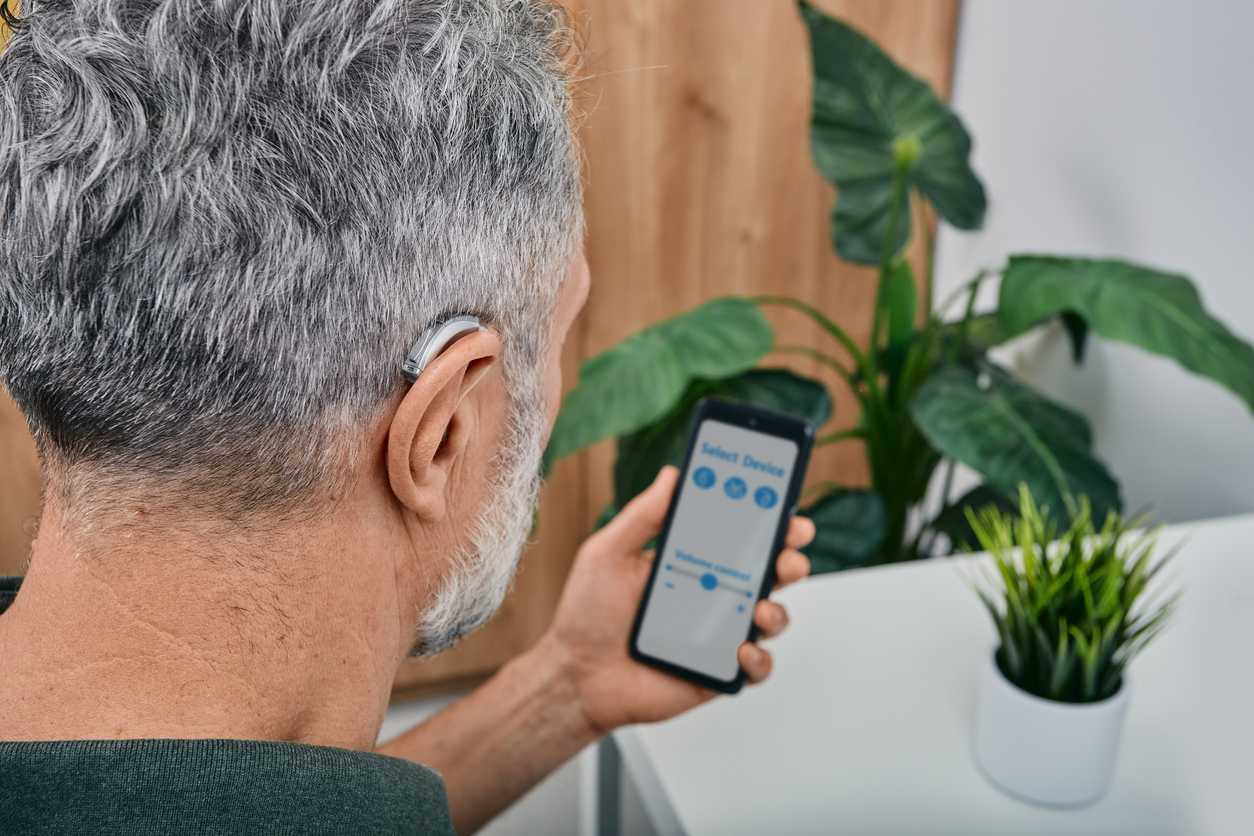 Senior man with a hearing aid pairing his device with his phone.