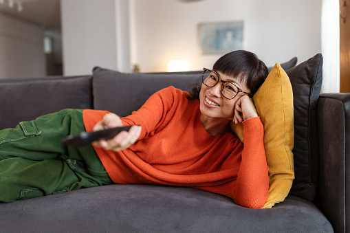 Smiling woman laying on her couch holding her TV remote.