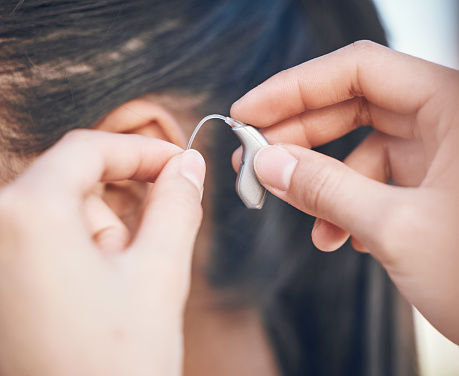 Hands positioning a hearing aid behind someone's ear.