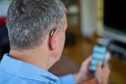 Senior man wearing a hearing aid, using his phone.